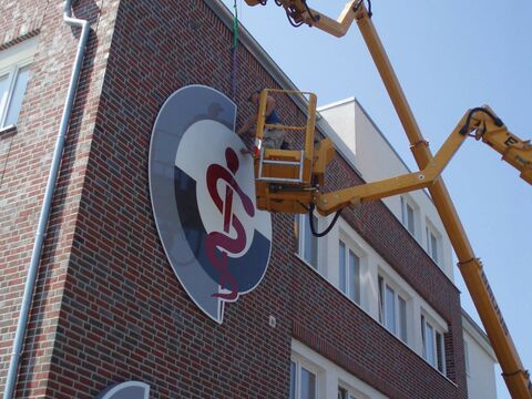 Ein großes Schild einer Firma wird an ein Gebäude angebracht